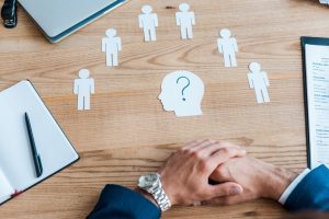 cropped view of recruiter with clenched hands near paper human shapes on table